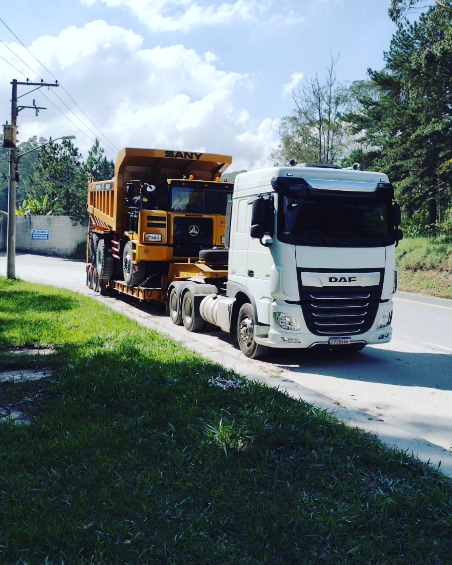Caminhão DAF branco com carreta prancha amarela transportando caminhão basculante SANY em rodovia de São Paulo
