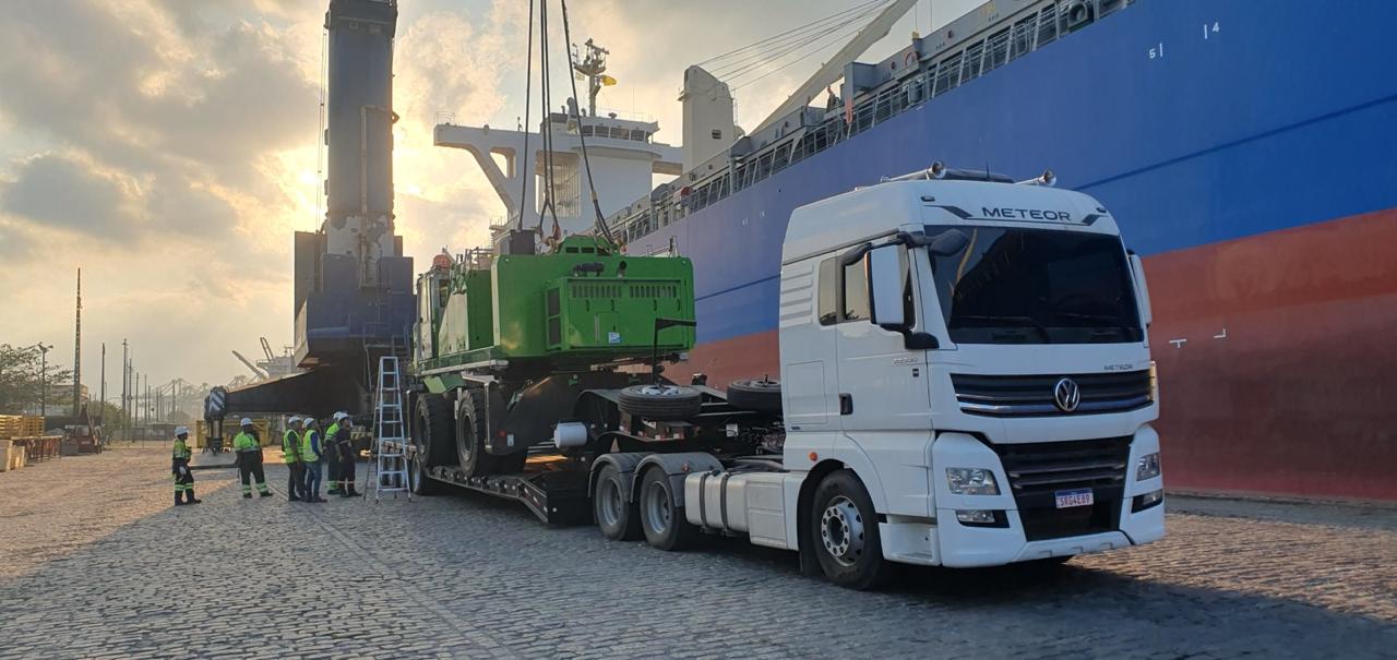 Caminhão do Grupo Correia retirando equipamento importado em porto nacional, ao lado de navio cargueiro