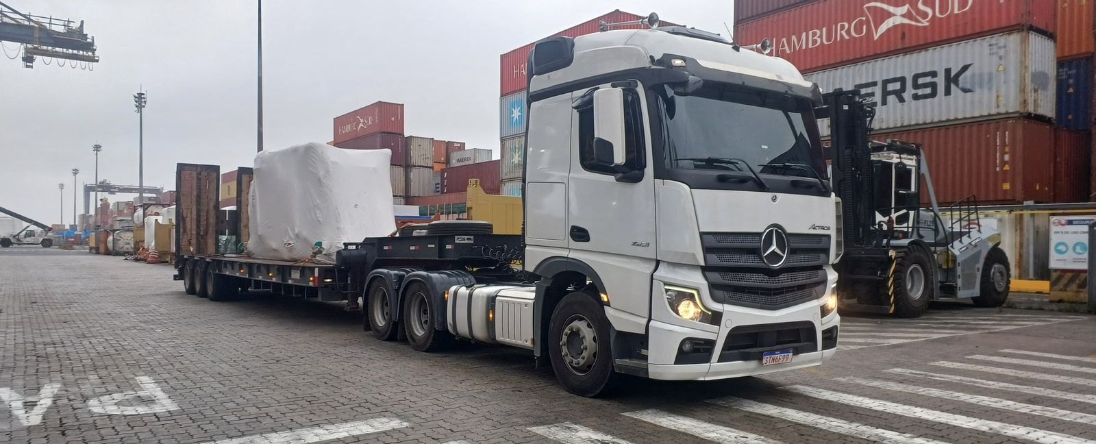 Caminhão Actros com carreta reta com rampas transportando carga industrial embalada em porto