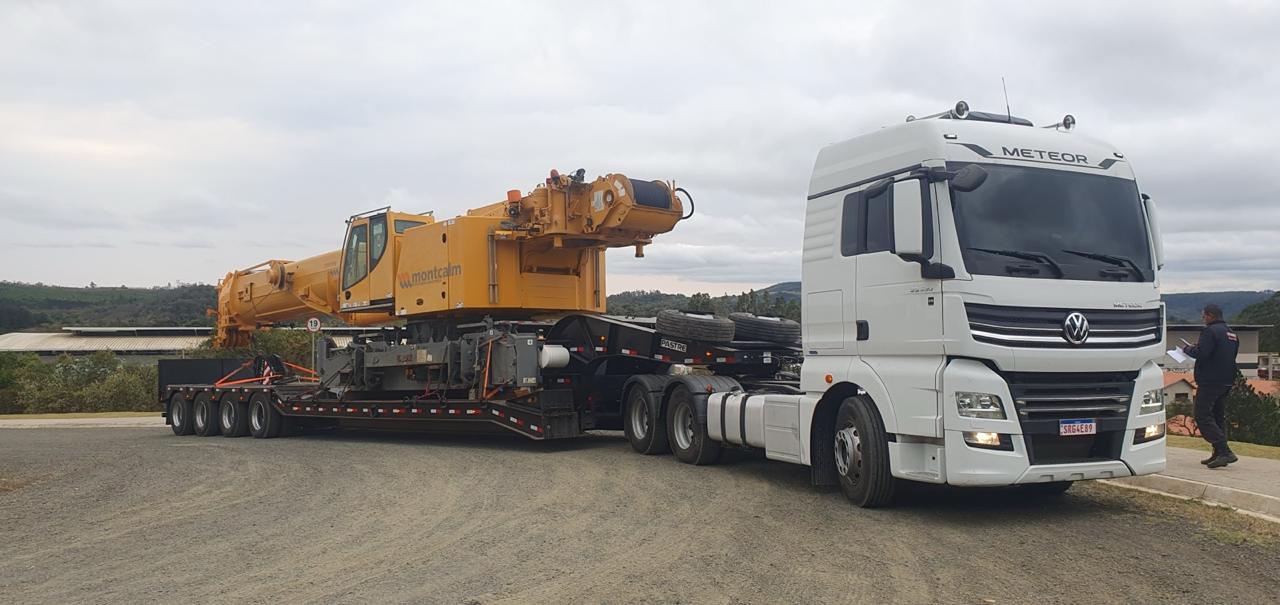 Caminhão Meteor com carreta pescoço hidráulico rebaixada transportando guindaste de 50 toneladas