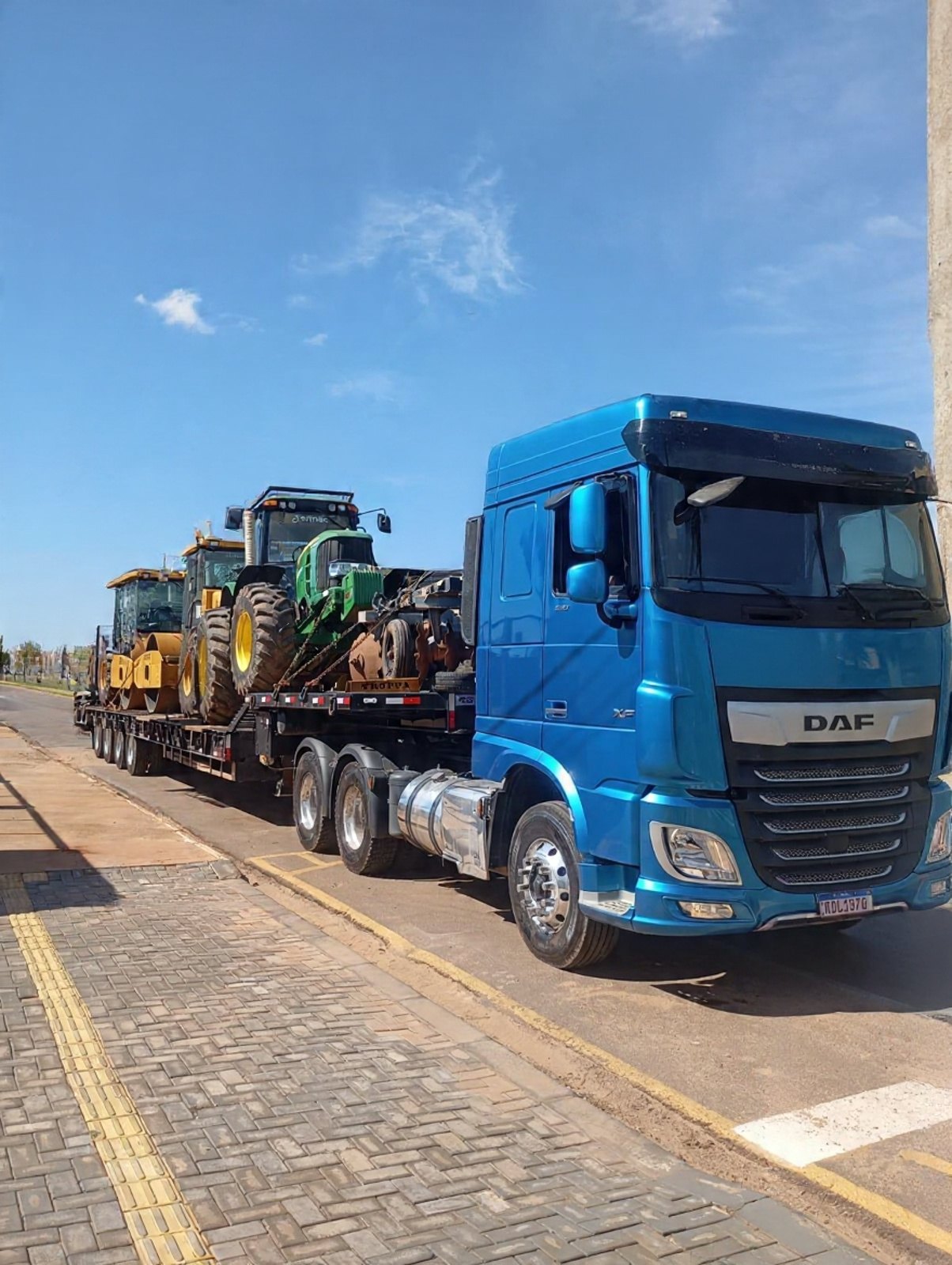 Caminhão DAF azul do Grupo Correia com carreta prancha transportando tratores e máquinas agrícolas
